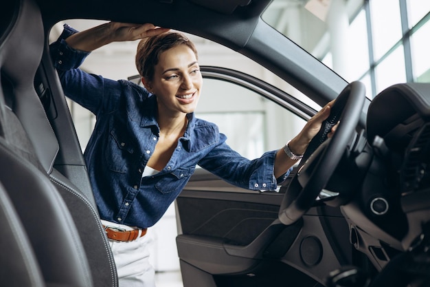 Jeune femme choisissant une voiture au showroom automobile