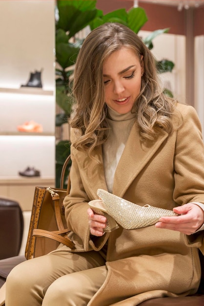 Une jeune femme choisit des chaussures élégantes dans une boutique Belle blonde dans un élégant manteau beige Vertical