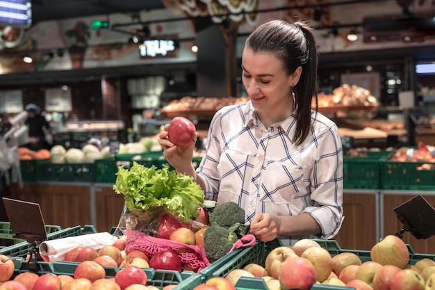 Une jeune femme choisit des fruits et légumes dans un supermarché