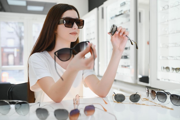 Jeune femme choisit des lunettes de soleil pour elle-même dans un magasin d'optique