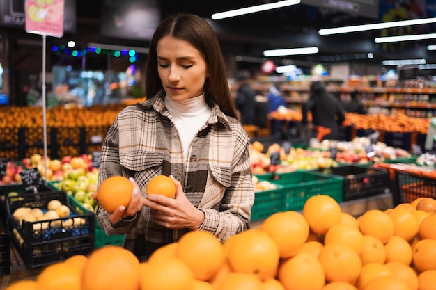 La jeune femme choisit des oranges dans le supermarché