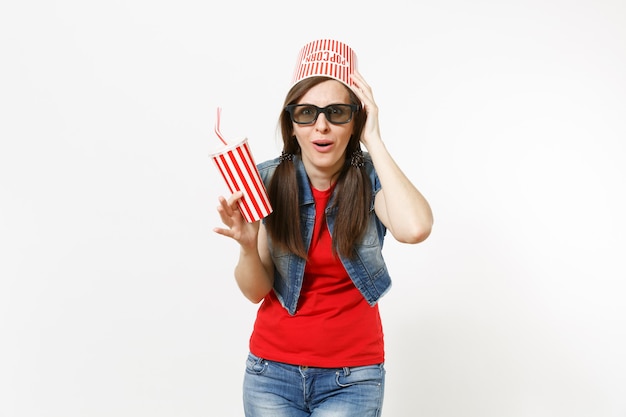 Jeune Femme Choquée Dans Des Lunettes 3d Avec Seau Pour Pop-corn Sur La Tête En Regardant Un Film, Tenant Une Tasse En Plastique De Soda Ou De Cola, Accrochée à La Tête Isolée Sur Fond Blanc. émotions Dans Le Concept De Cinéma.