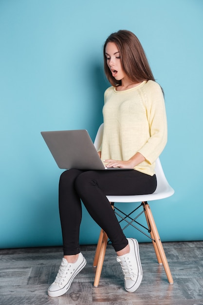 Jeune femme choquée regardant l'écran d'ordinateur portable isolé sur fond bleu