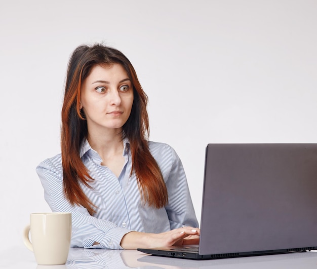 Jeune femme choquée travaillant avec l'ordinateur