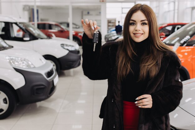 Une jeune femme avec les clés de sa nouvelle voiture dans un magasin de voitures