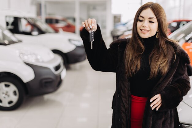 Une jeune femme avec les clés de sa nouvelle voiture dans un magasin de voitures