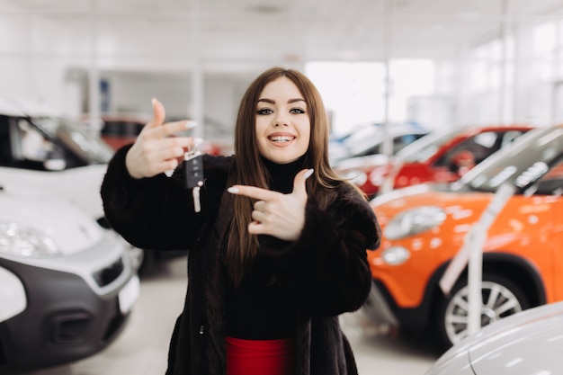 Une jeune femme avec les clés de sa nouvelle voiture dans un magasin de voitures