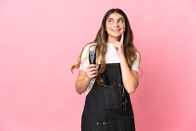 Jeune femme de coiffeur isolée sur un mur rose en pensant à une idée tout en levant