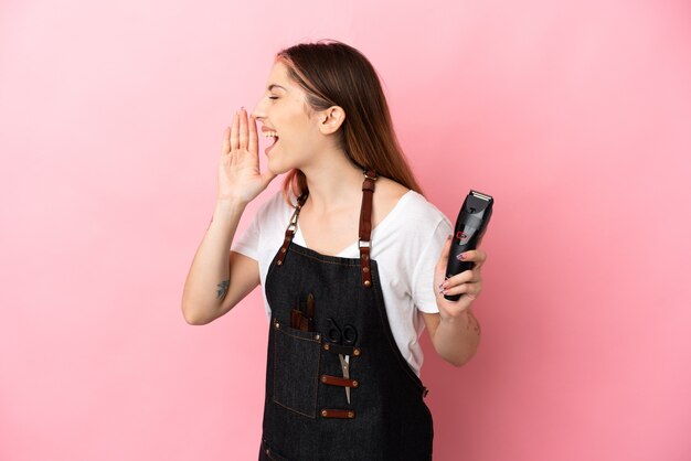 Jeune femme de coiffeur isolée sur rose en criant avec la bouche grande ouverte sur le côté