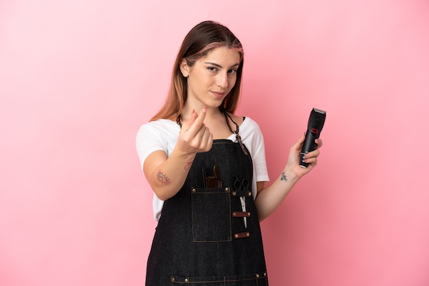 Jeune femme de coiffeur isolée sur rose faisant le geste de l'argent