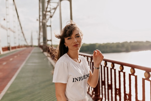 Jeune femme avec une coiffure longue et un tshirt blanc habillé se promène dans la ville Portrait en plein air de femme passant du temps libre