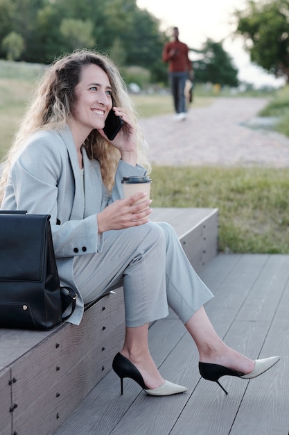 Jeune femme col blanc buvant et parlant sur smartphone