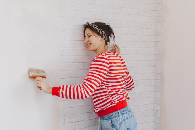 Une jeune femme colle du papier peint à la maison. fille colle du papier peint sous la forme d'une brique. réparation.