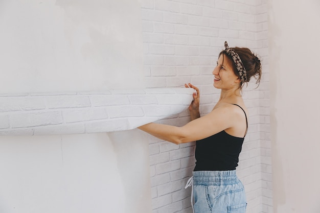 Une jeune femme colle du papier peint à la maison. fille colle du papier peint sous la forme d'une brique. réparation.