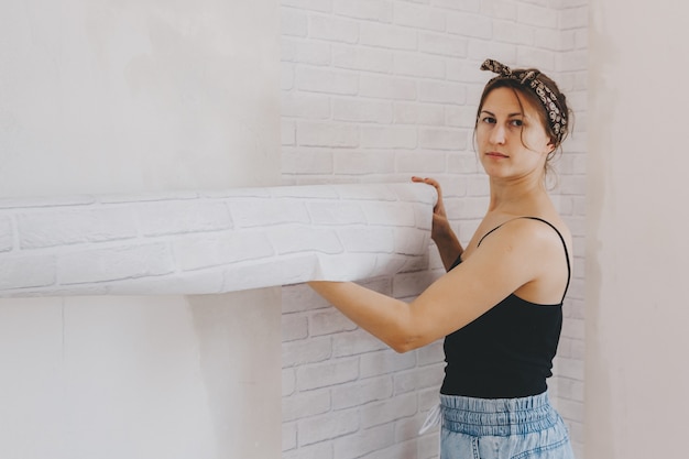 Une jeune femme colle du papier peint à la maison. fille colle du papier peint sous la forme d'une brique. réparation.