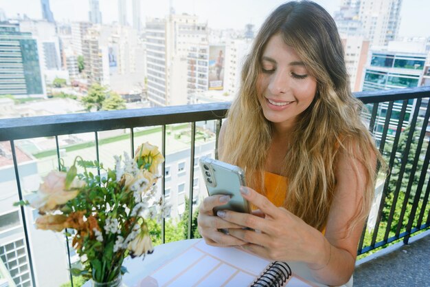 Jeune femme colombienne latine assise dans son appartement en souriant et en vérifiant les médias sociaux sur son téléphone