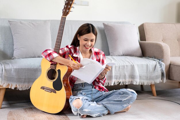 Photo une jeune femme compose une chanson et écrit des paroles sur un cahier tout en mettant la guitare sur les jambes et en s'asseyant