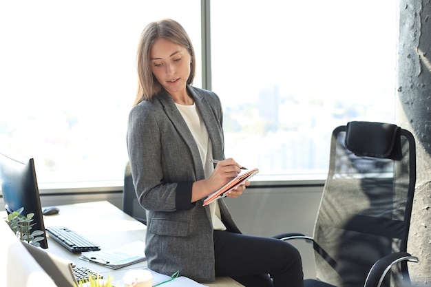 Jeune femme concentrée écrivant quelque chose tout en travaillant au bureau.