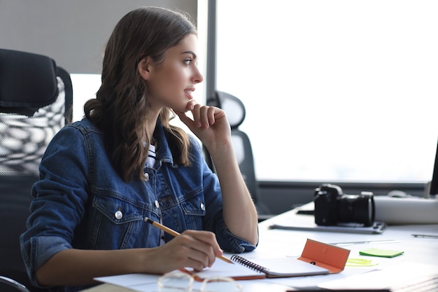 Jeune femme concentrée écrivant quelque chose tout en travaillant au bureau.