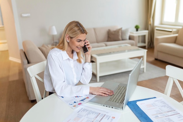 Jeune femme concentrée à la maison faisant un appel d'affaires à l'aide d'un ordinateur portable Entrepreneur élégant blond travaillant à la maison Femme gérant les factures domestiques et les finances de la maison