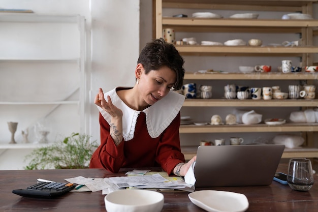 Jeune femme concentrée propriétaire d'un studio de céramique analysant les factures et les reçus faisant l'analyse des coûts de la poterie