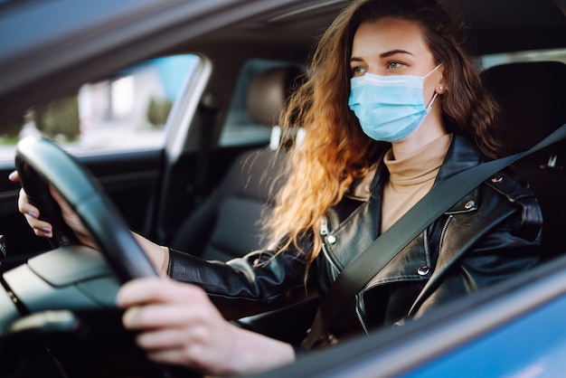 Jeune femme conduisant une voiture portant un masque médical lors d'une épidémie. Isolement des transports. Covid-2019.