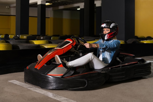 Une jeune femme conduit une voiture de kart avec de la vitesse dans une piste de course de terrain de jeu. Le kart est un sport automobile de loisir populaire