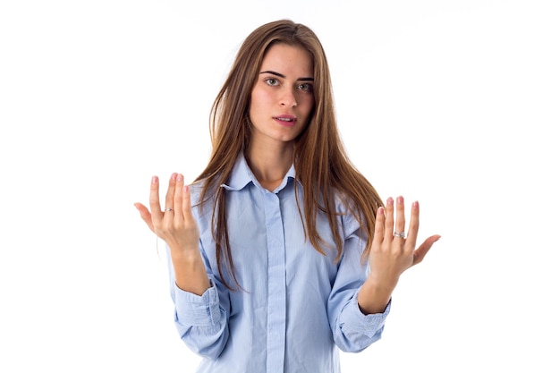 Jeune femme confiante aux cheveux longs en chemise bleue montrant ses mains sur fond blanc en studio