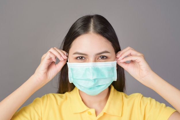 Jeune femme confiante en chemise jaune porte un masque chirurgical sur gris