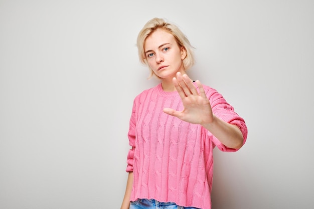 Photo une jeune femme confiante en pull rose montrant un geste d'arrêt avec la main sur un fond clair