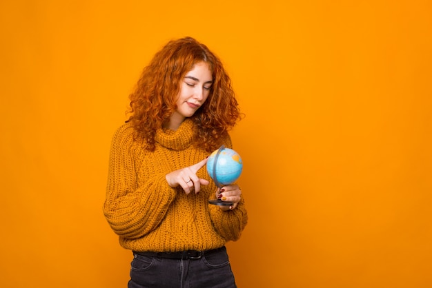 Une jeune femme confuse regarde le globe près d'un fond orange.