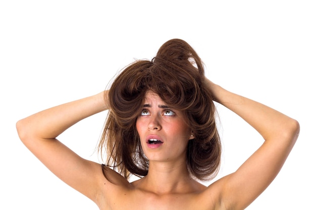Jeune femme confuse tenant ses longs cheveux bruns emmêlés sur fond blanc en studio