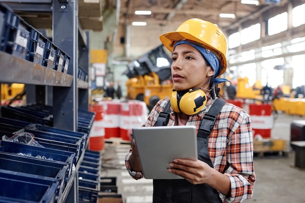 Jeune femme constructeur avec tablette debout près d'une étagère avec des conteneurs