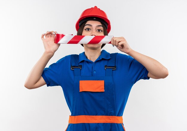 Jeune femme de constructeur en uniforme bouche couverte de ruban adhésif isolé sur mur blanc