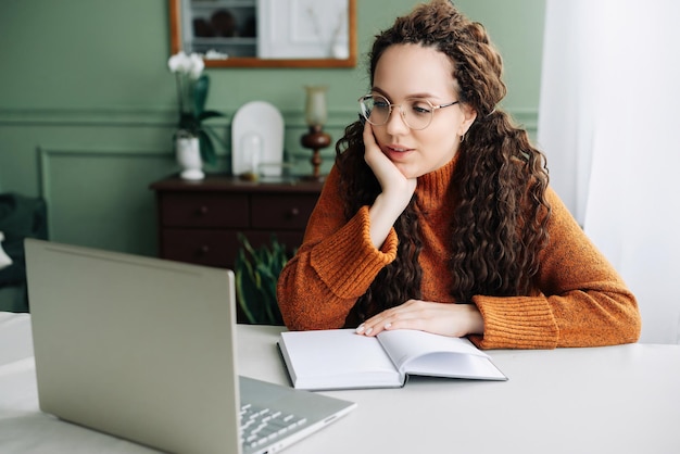 Jeune femme contemplative prenant des pauses dans l'apprentissage en ligne et travaillant sur un ordinateur portable à la maison Jeune femme étudiant et travaillant à domicile perdue dans ses pensées et contemplant des idées sur son ordinateur portable