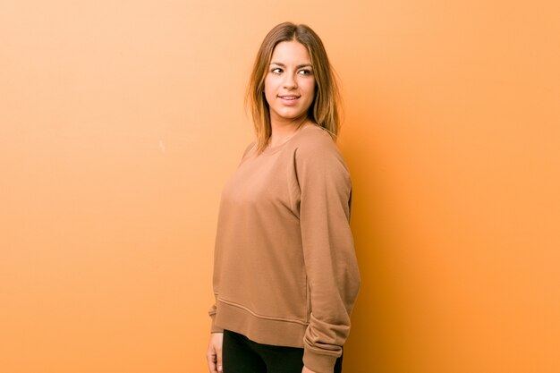 Jeune femme contre un mur regarde de côté souriant, gai et agréable.