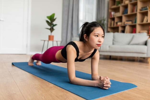 Jeune femme coréenne debout en position de planche sur un tapis de yoga faisant de l'exercice à la maison à l'intérieur du salon