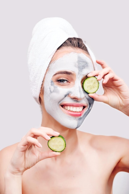 Jeune femme avec des cosmétiques sur le visage appliquant du concombre à l'œil