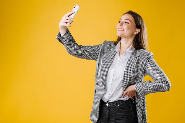 Jeune femme en costume à l'aide d'un smartphone sur fond jaune