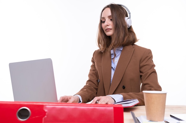 Jeune femme en costume marron et chemise blanche boit du café et travaille sur un ordinateur portable sur fond blanc isolé