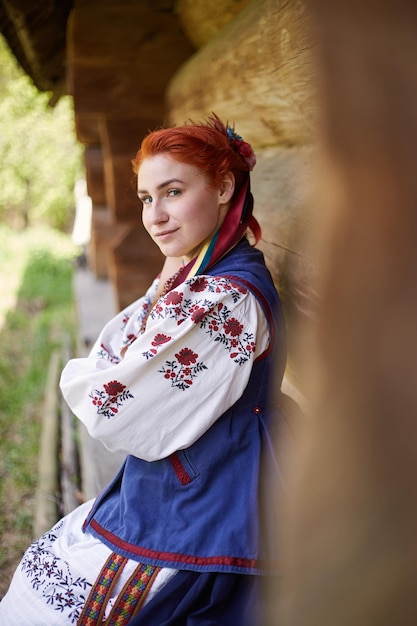 Jeune femme en costume national ukrainien Jeune femme souriante en vêtements traditionnels près de la vieille maison en bois Paix en Ukraine