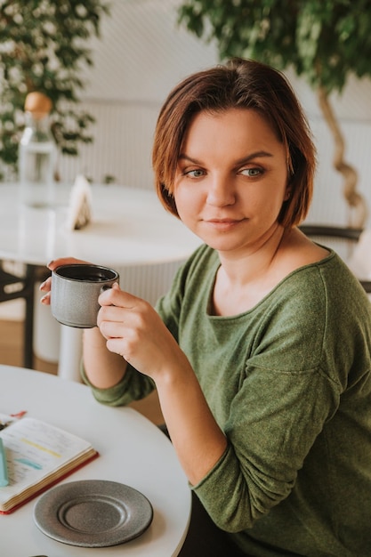 Une jeune femme avec une coupe de cheveux courte est assise dans un café et boit du thé