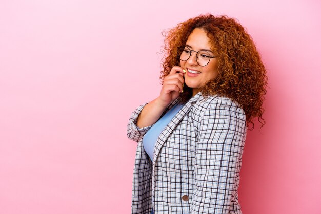 Jeune femme courbée latine isolée sur fond rose détendu penser à quelque chose en regardant un espace de copie.