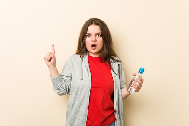 Jeune femme courbée taille plus tenant une bouteille d'eau ayant une excellente idée, concept de créativité.