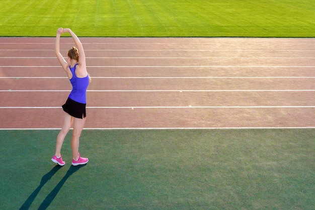 Jeune femme coureur qui s'étend avant de courir sur la piste du stade