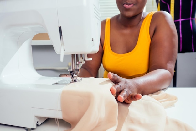 Jeune femme couturière afro-américaine coud des vêtements sur une machine à coudre au bureau de tailleur dans un style d'été tropical.