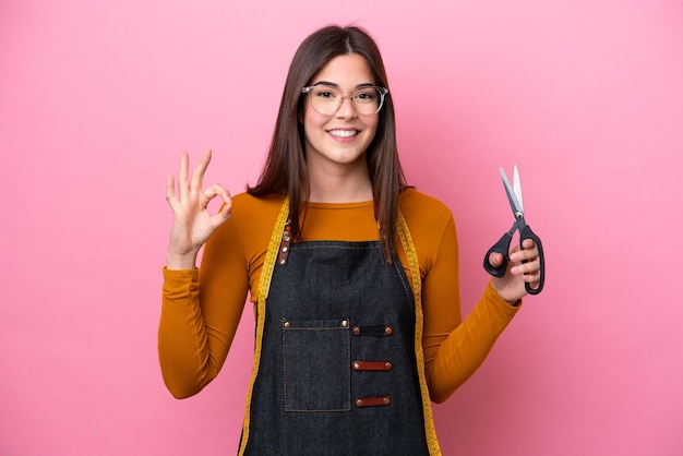 Jeune femme couturière brésilienne isolée sur fond rose montrant un signe ok avec les doigts