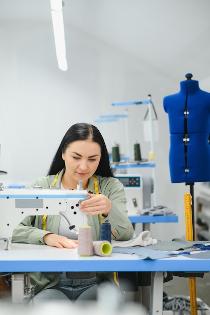 Jeune femme couturière coud des vêtements sur la table de travail Couturière souriante et sa main se bouchent dans l'atelier