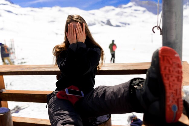 Jeune femme a couvert son visage avec ses mains et des sièges à côté des montagnes en hiver