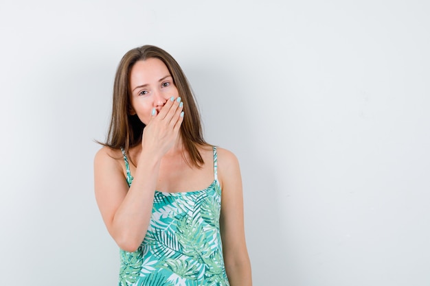 Jeune femme couvrant la bouche avec la main en chemisier et l'air sérieux. vue de face.